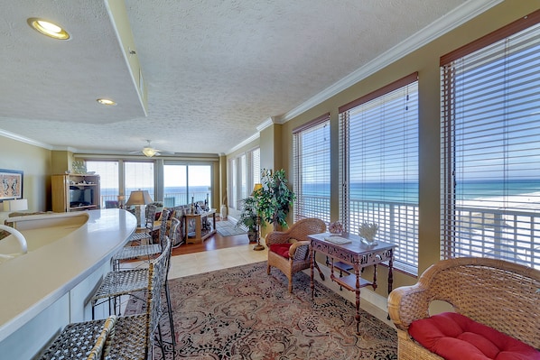 A spacious living area with a view of the ocean, a bar, and a dining area with wicker furniture.