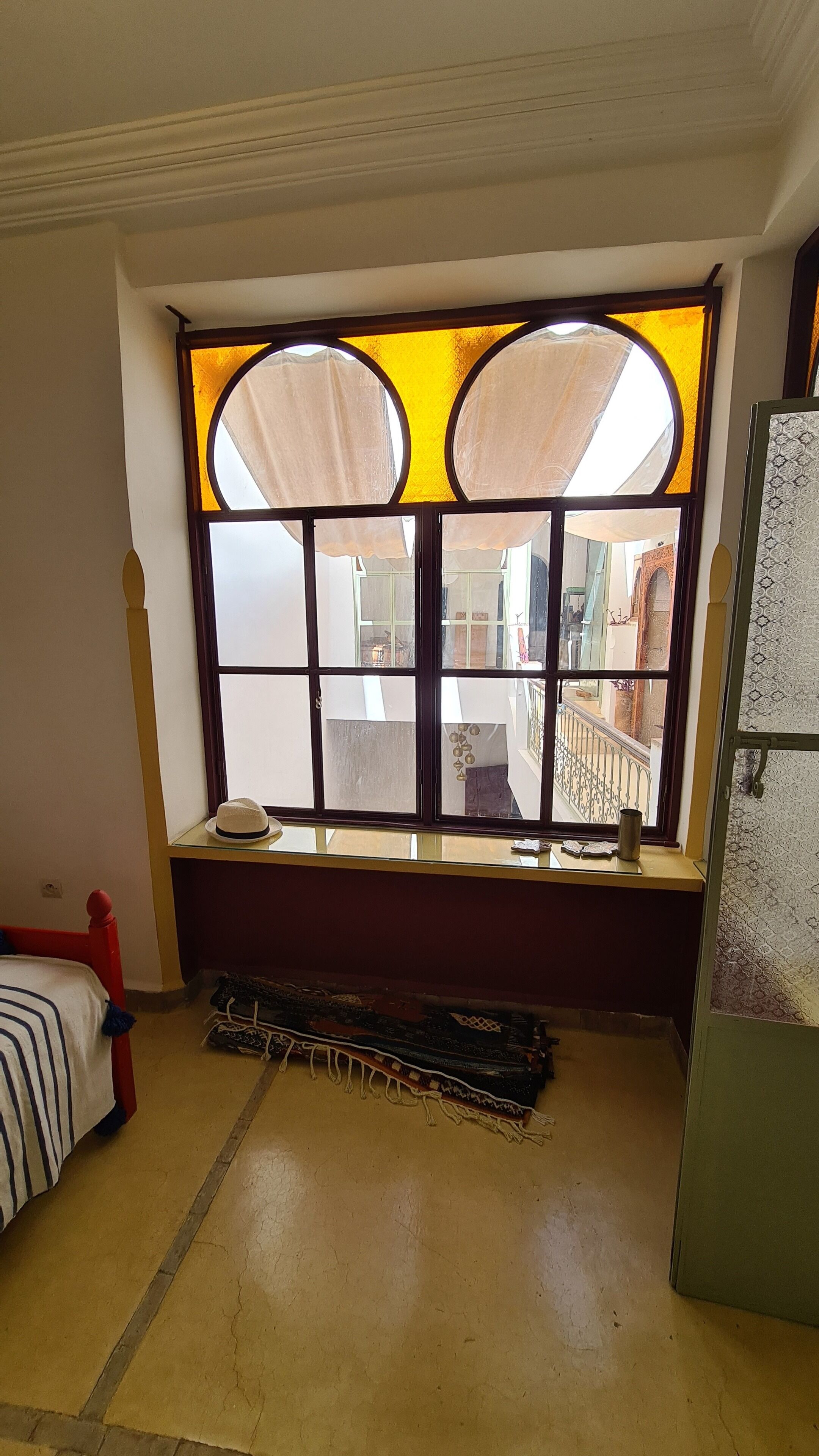 Ein Zimmer mit großem Fenster, einem Bett, einem kleinen Tisch und einem Kühlschrank.