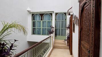 A narrow corridor with a white wall, a wooden door with intricate carvings, and a metal railing.