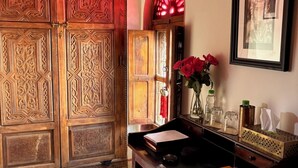A room with a wooden door, a desk with a vase of red flowers, and a framed picture on the wall. - Riad La Cigale (Marrakech)