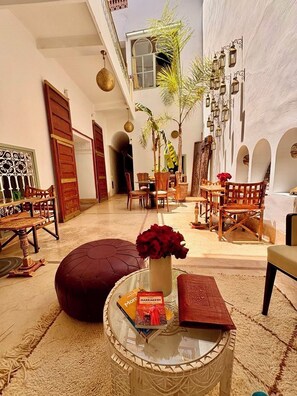 Un patio amplio con una mesa redonda de vidrio, rosas rojas y un libro titulado 'Marrakesh'.