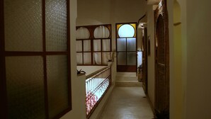 A narrow, dimly lit hallway with a wooden door on the right, a window with a decorative frame on the left, and a staircase leading to an upper level. - Riad La Cigale (Marrakech)