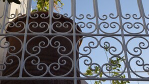 A metal railing with a decorative design, a potted plant with pink flowers, and a clear blue sky in the background. - Riad La Cigale (Marrakech)