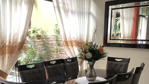A dining area with a glass-top table surrounded by six chairs, a vase with flowers, and a large mirror on the wall. - B&B Cusing Wasi (Callao)