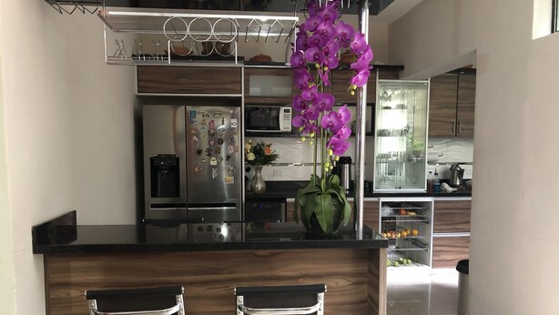 A modern kitchen with a central island, two bar stools, a refrigerator with magnets, a microwave, and a vase with flowers. - B&B Cusing Wasi (Callao)