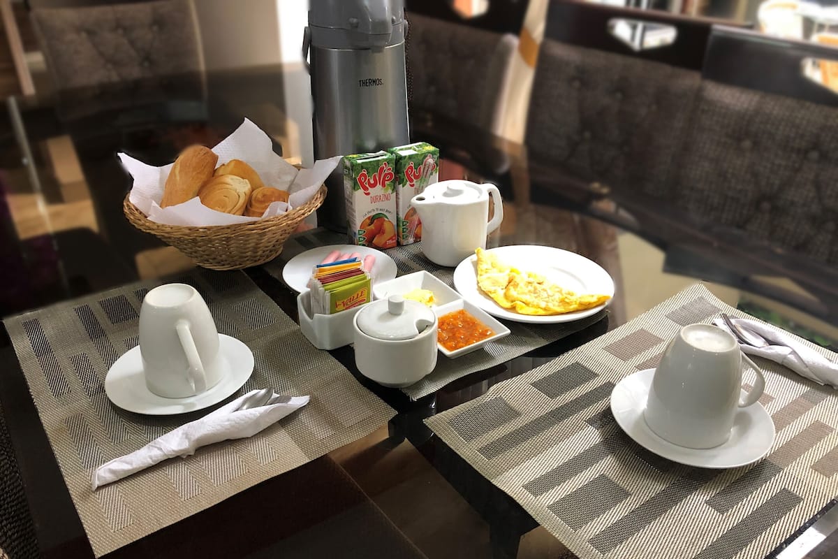 A breakfast table with croissants, a thermos, juice cartons, a teapot, and a plate of eggs.
