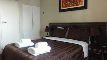 A hotel room with a large bed, two bedside lamps, a painting on the wall, and a wardrobe.