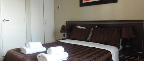 A hotel room with a large bed, two bedside lamps, a painting on the wall, and a wardrobe.