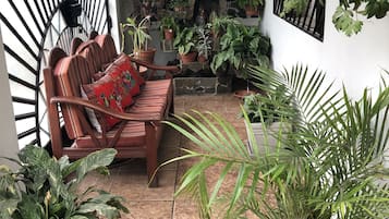 A cozy patio area with a wooden bench and cushions, surrounded by various potted plants and a stone fireplace.