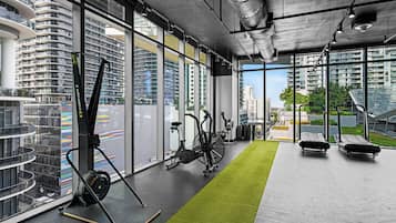 A modern gym with exercise equipment, large windows, and a view of high-rise buildings.