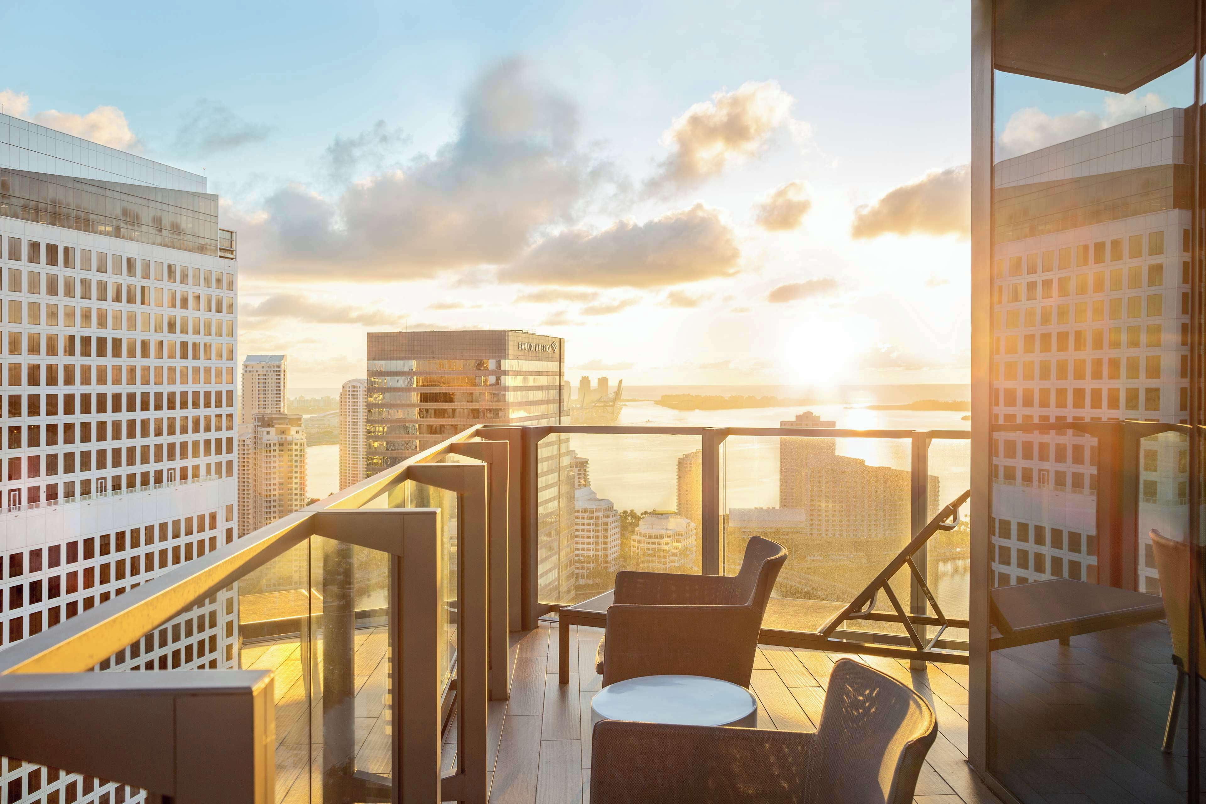 A high-rise building with a glass balcony overlooking a cityscape during sunset.