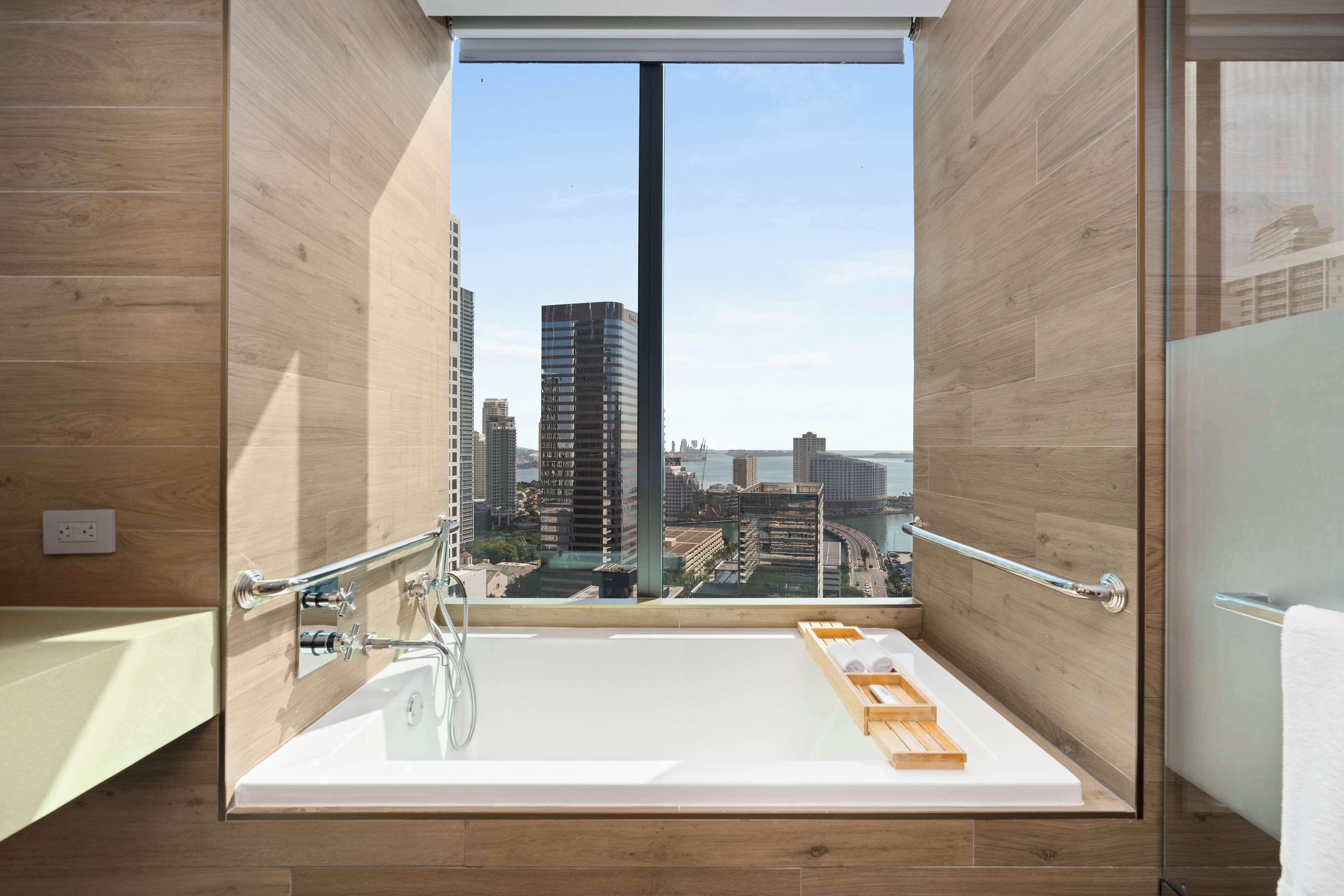 Un baño moderno con una bañera grande, paredes de madera y vistas a la ciudad.