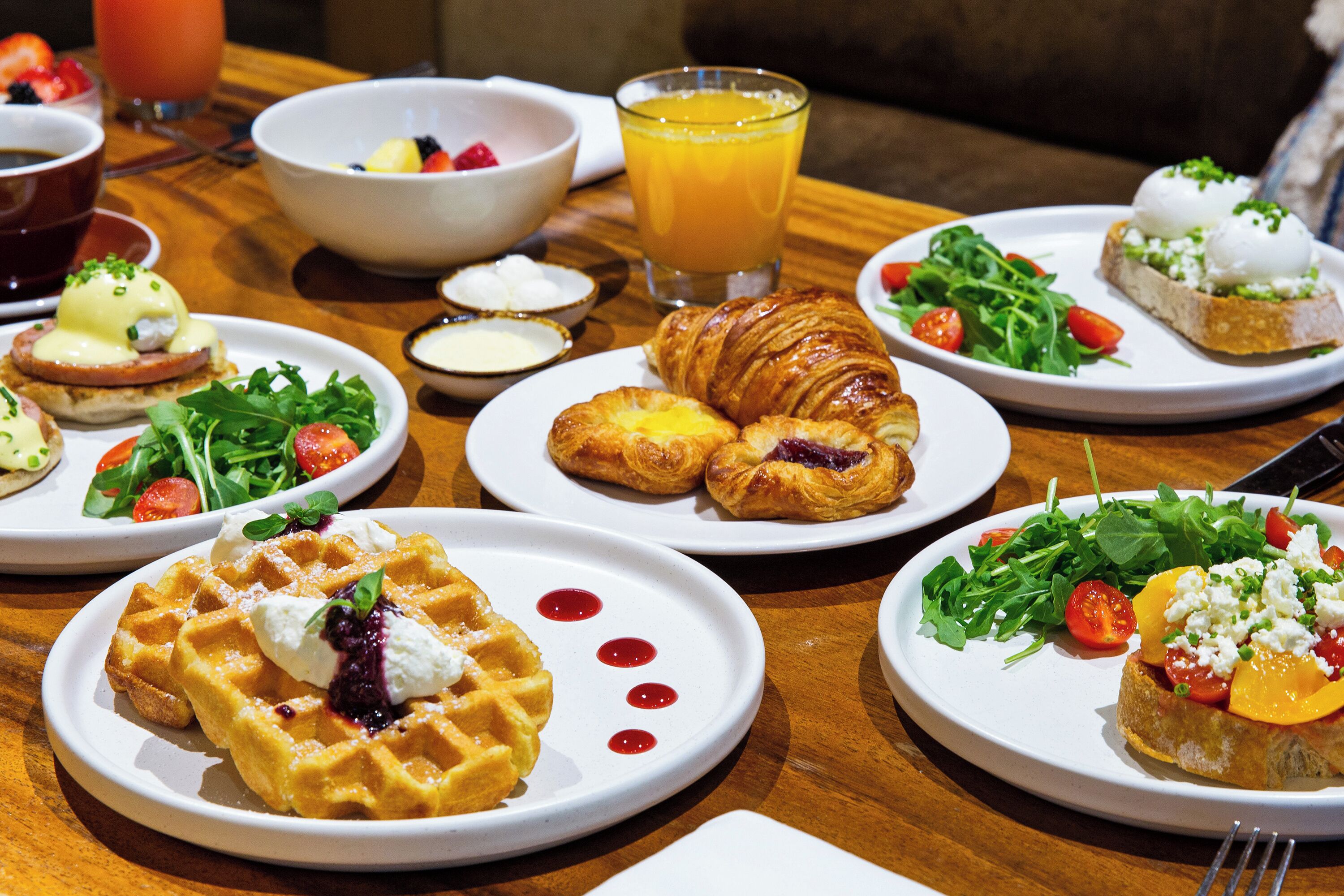 Una mesa de desayuno con diferentes platos, incluyendo gofres, cruasanes y una ensalada.