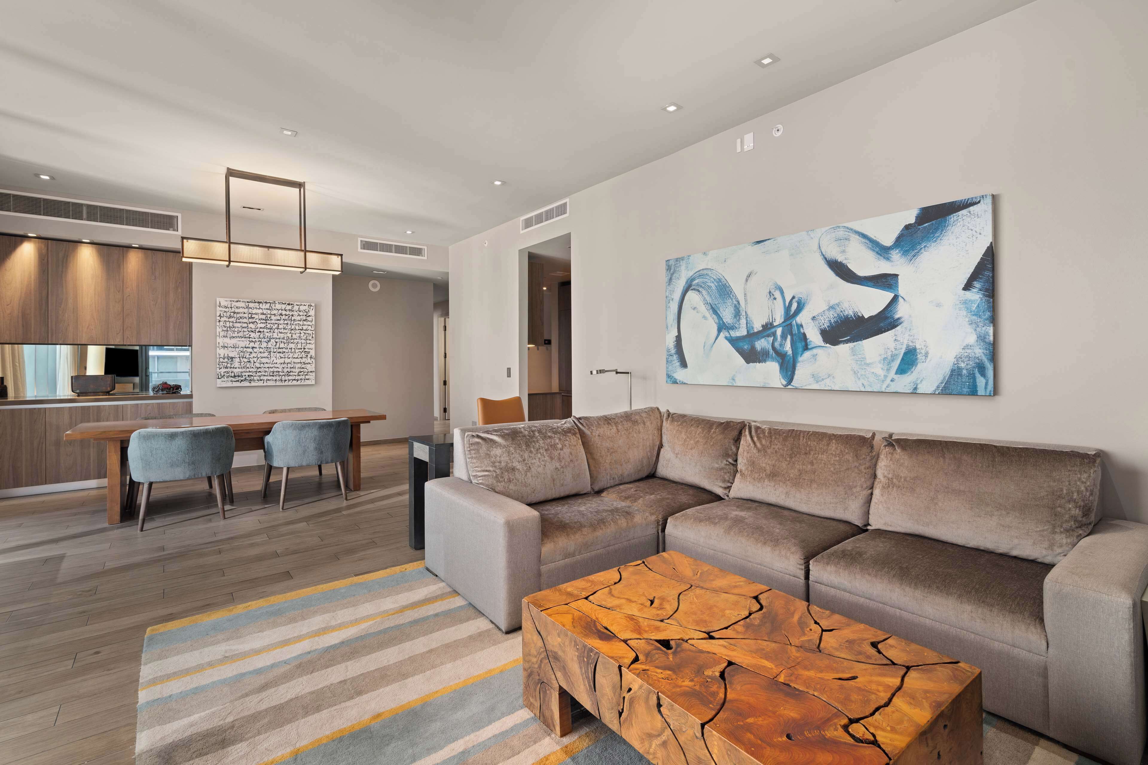 A modern living room with a sectional sofa, a coffee table, and a large abstract painting on the wall.
