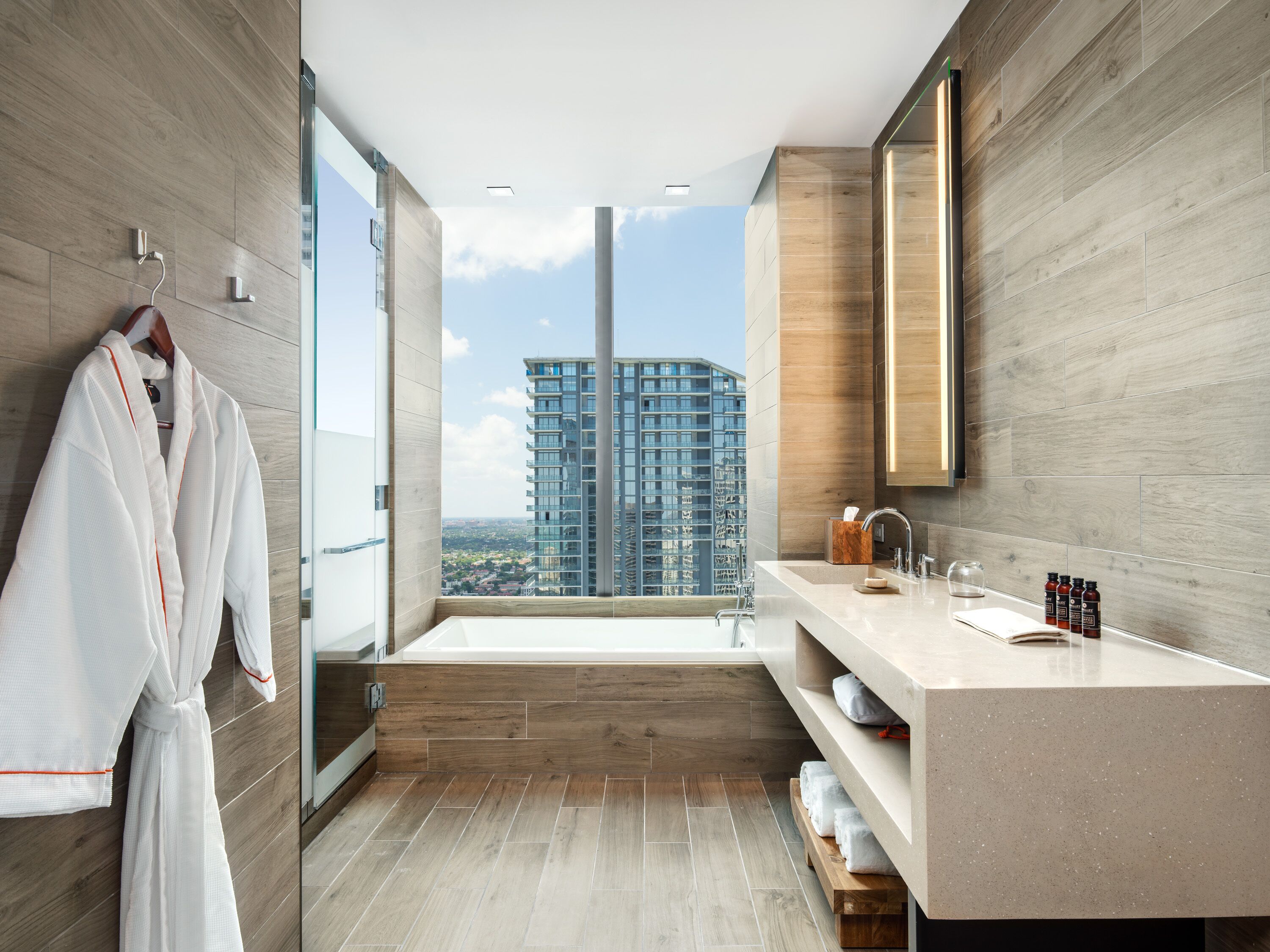 A modern bathroom with a large bathtub, a vanity with a mirror, and a robe hanging on the wall.