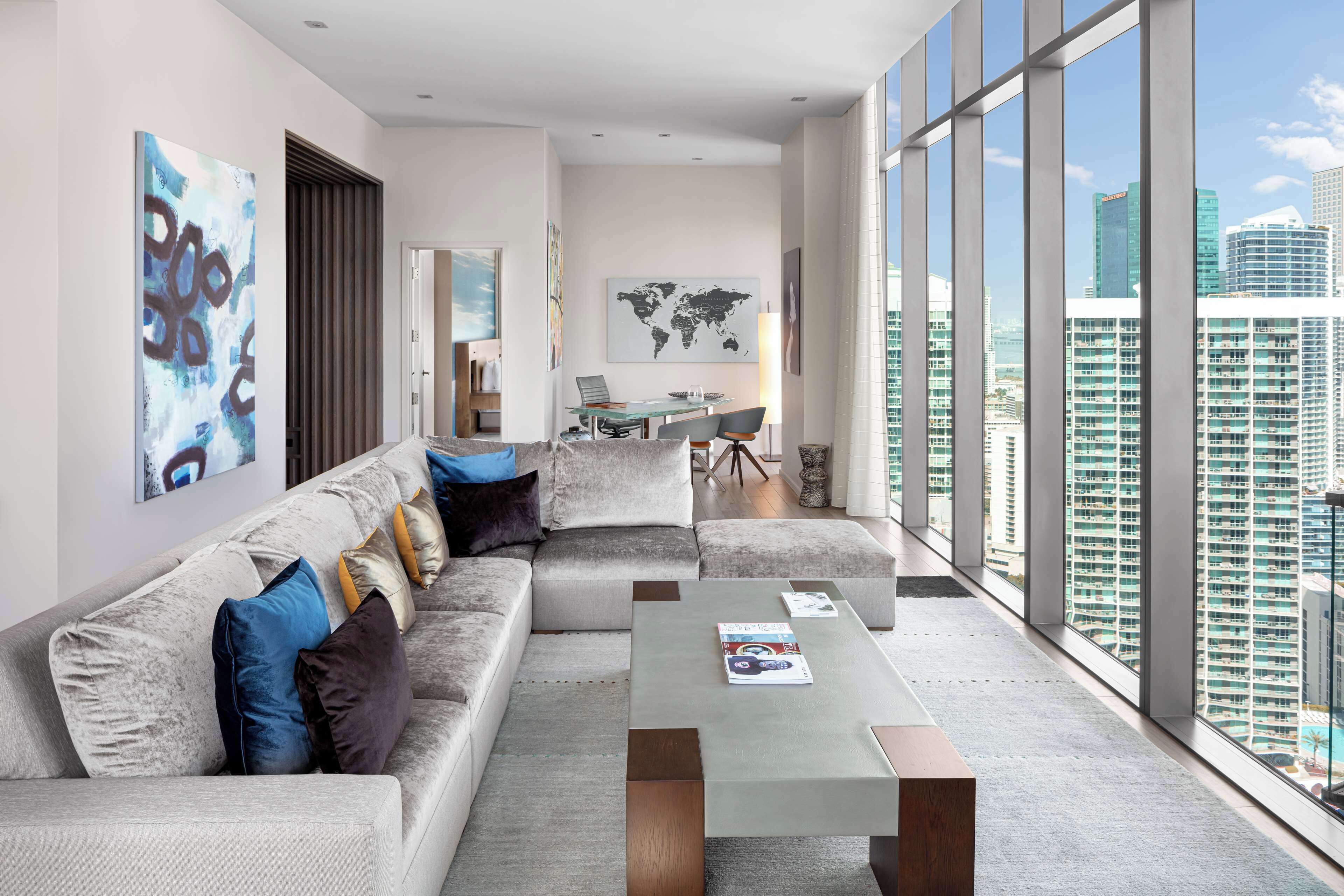 Ein modernes Wohnzimmer mit einer Couch, einem Couchtisch und Blick auf eine Stadtkulisse durch große Fenster.