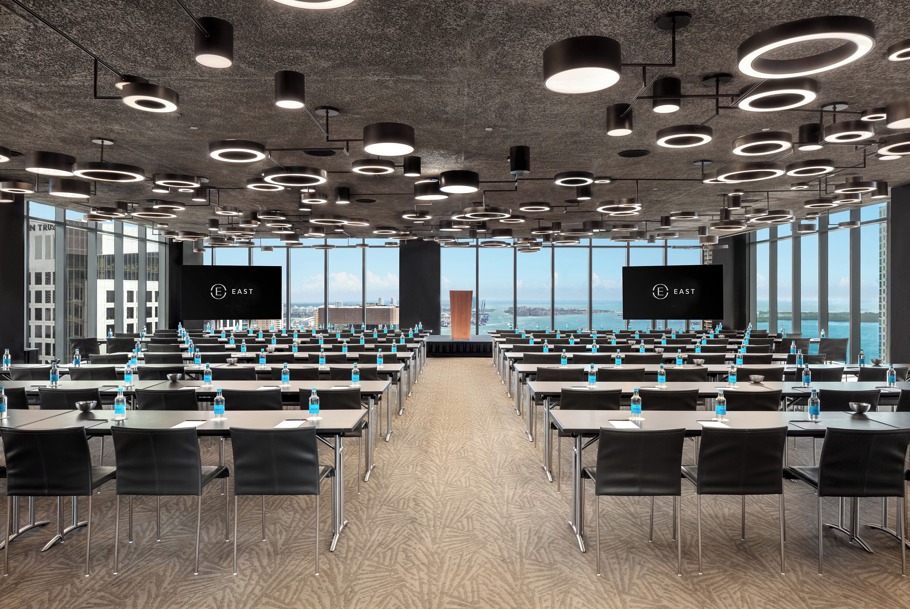 A conference room with multiple tables and chairs, large windows, and a view of the city.