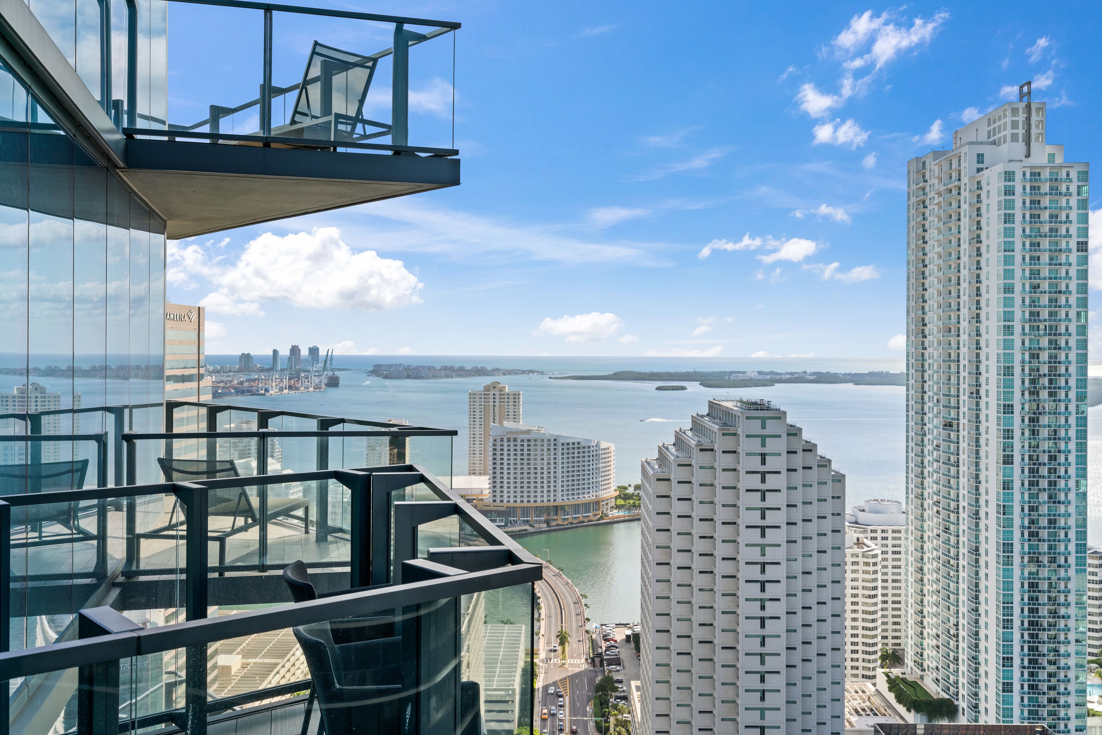 A high-rise building with a glass balcony overlooking a cityscape and a body of water.