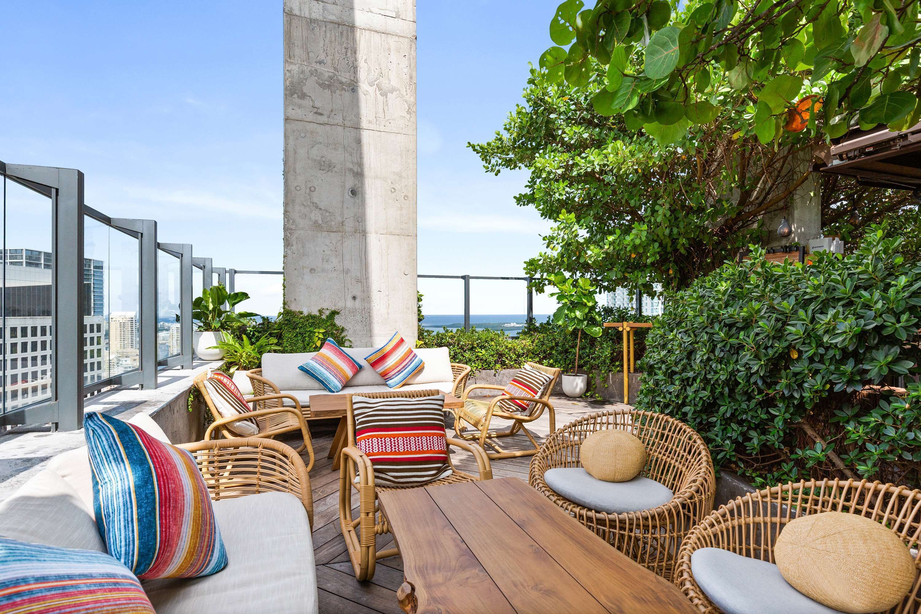 A rooftop terrace with wicker furniture, cushions, and a view of the city.