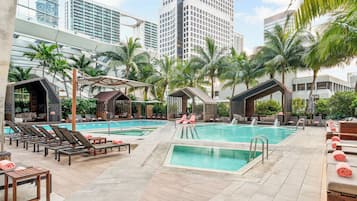 Un área de piscina en la azotea con varias piscinas, sillones de descanso y palmeras.