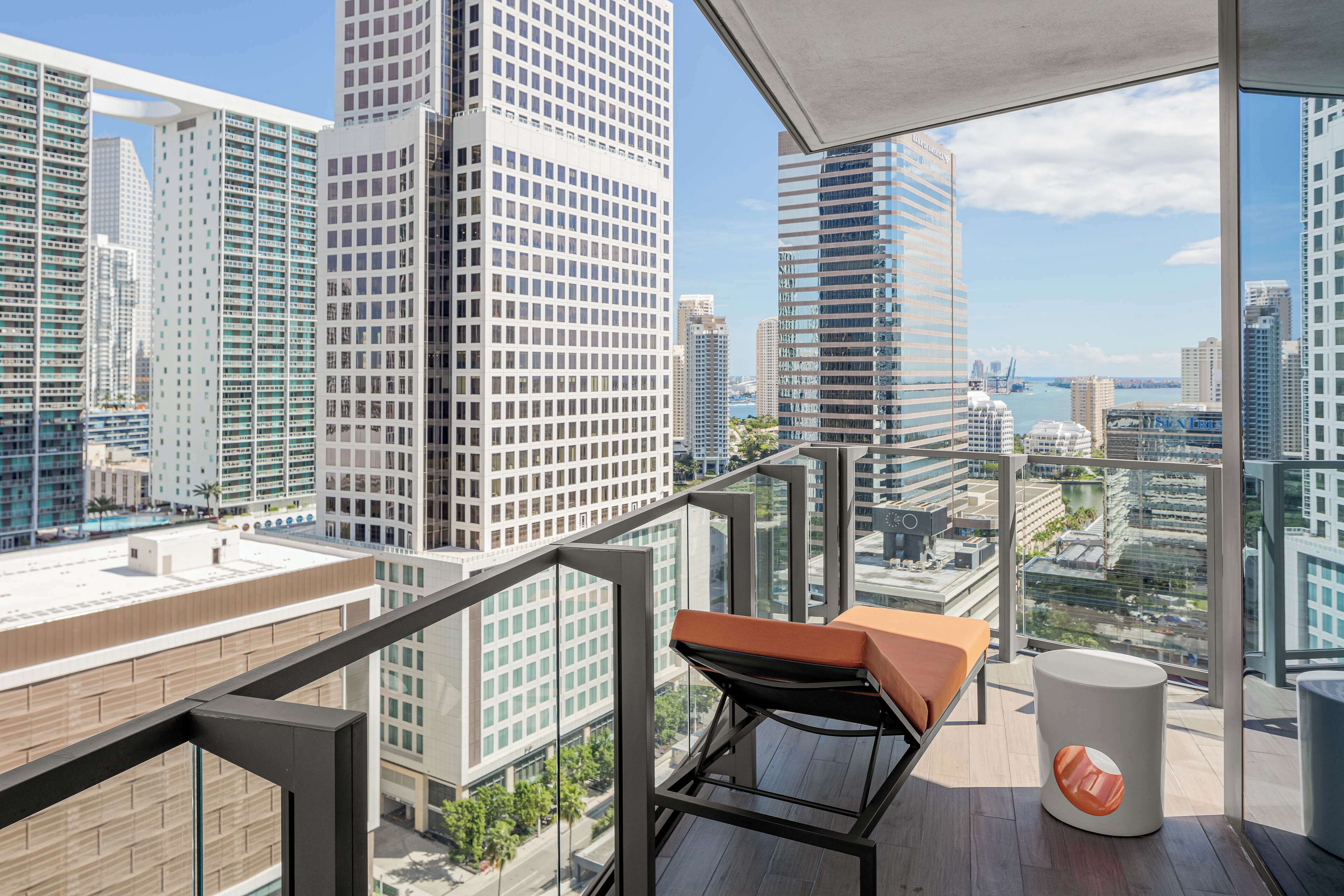 A high-rise balcony with a view of city skyscrapers, a cushioned seating area, and a small table.