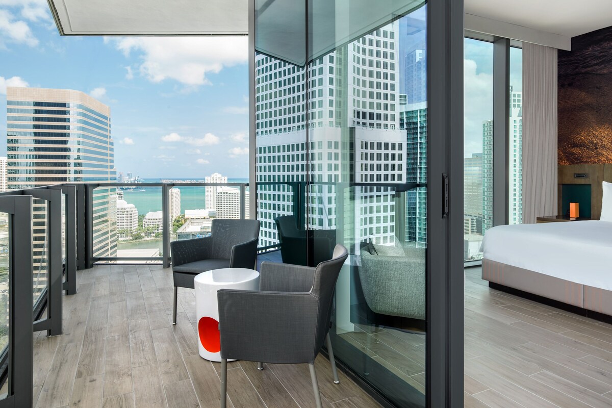 Una habitación de hotel moderna con balcón, ventanas amplias y vistas a la ciudad.