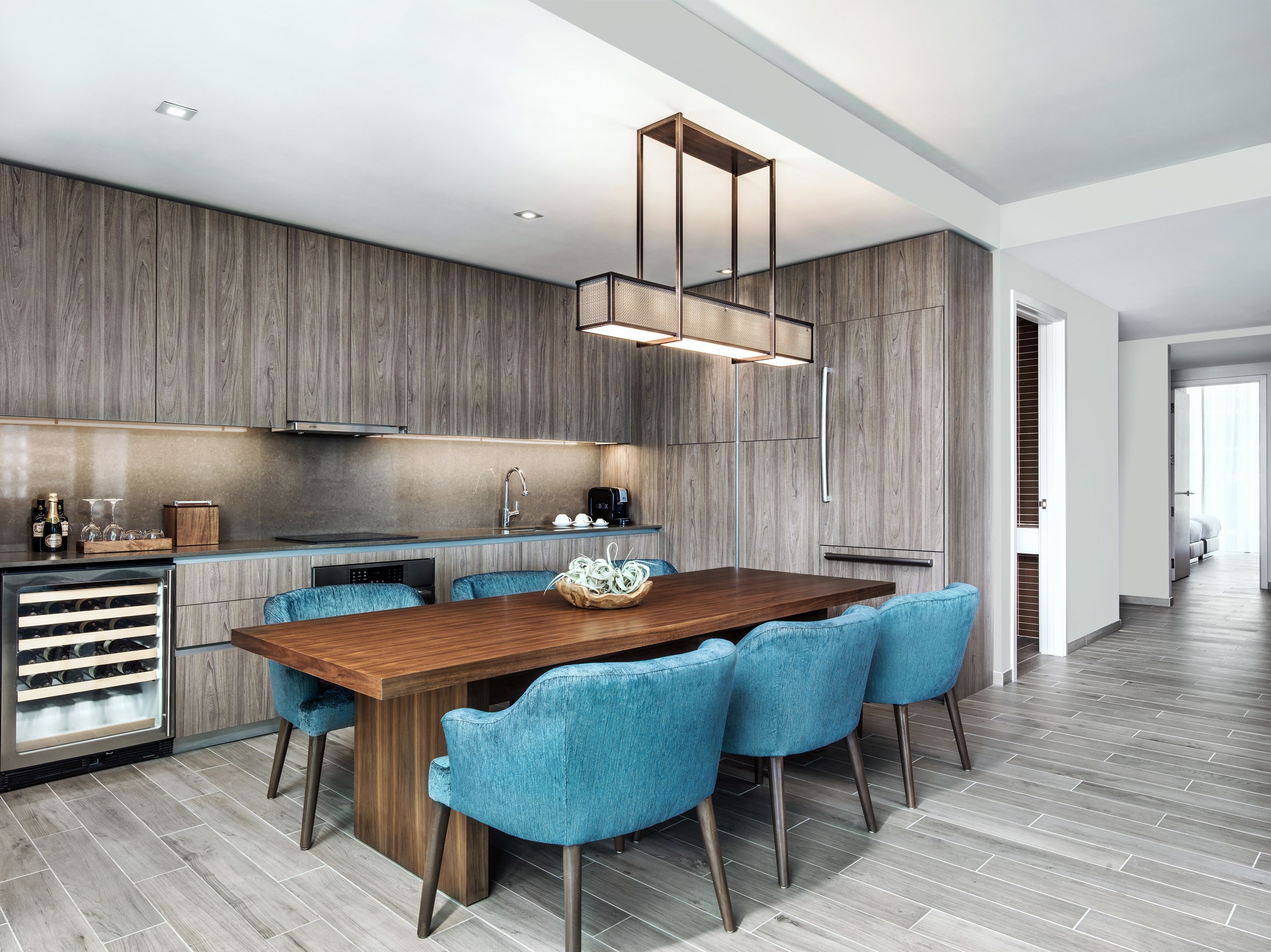 A modern kitchen with wooden cabinetry, a central island, and blue chairs.