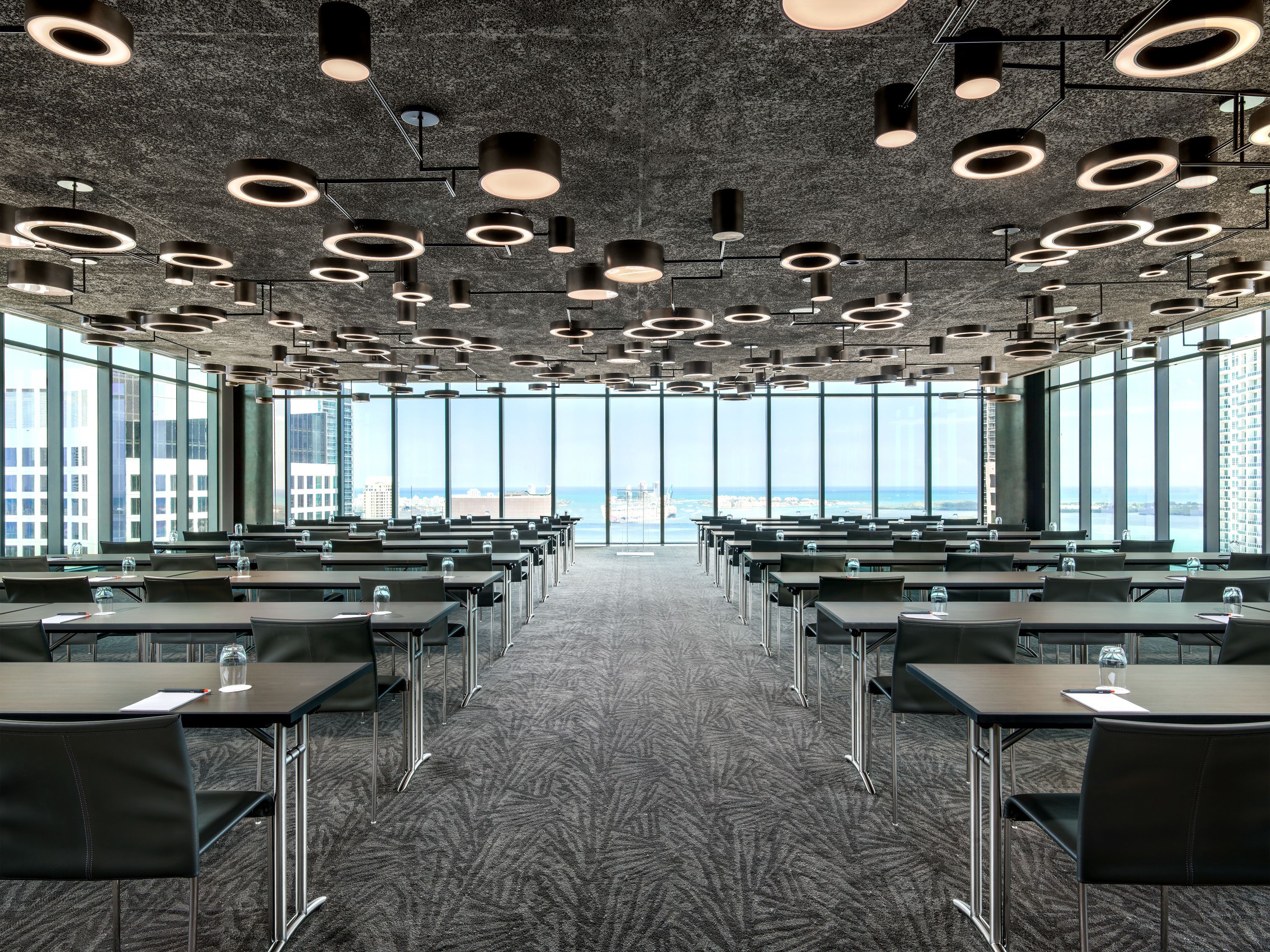 A conference room with a view of the city and ocean, featuring a modern ceiling design and carpeted floor.
