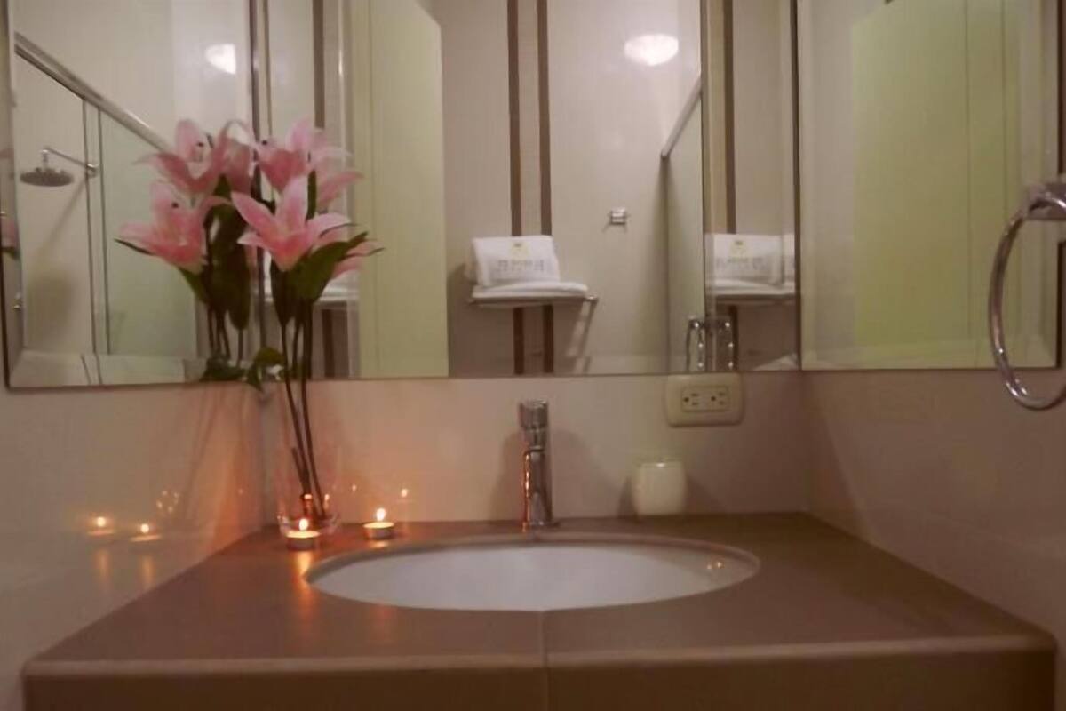 A bathroom with a sink, mirror, and a vase with flowers.