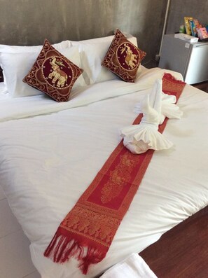 A neatly made bed with white linens, two decorative pillows, and a red and gold patterned throw.