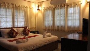 A hotel room with a large bed, two pillows, a bedside table, and a TV. - Racha Herb Gardens (Saraphi)