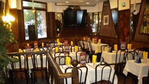 Un restaurant avec de nombreuses tables et chaises, chacune étant recouverte d’une nappe blanche et agrémentée de bougies jaunes.