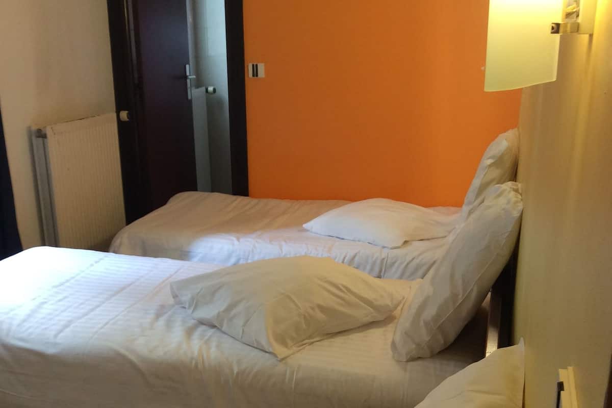 A hotel room with two beds, white bedding, an orange wall, and a door.