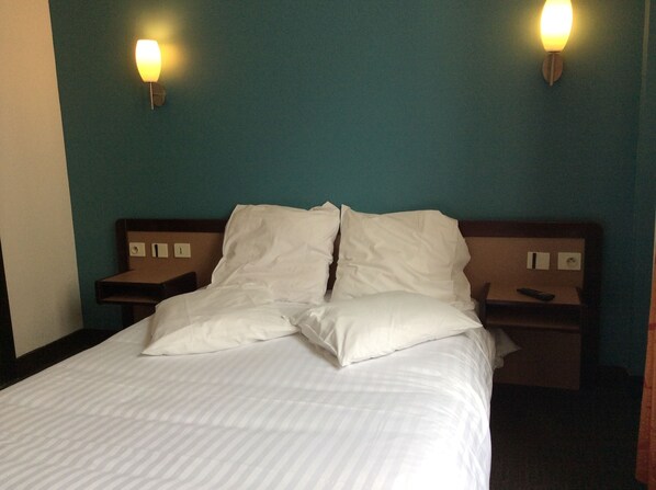 A hotel room with a bed, two bedside tables, and two wall-mounted lights. - Hotel De La Place (Malakoff)