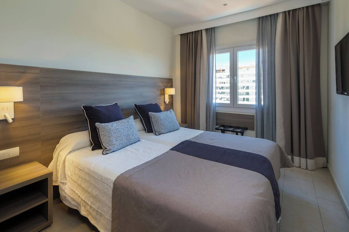 Een hotelkamer met een groot bed, twee nachtkastjes, een televisie en een raam met gordijnen.