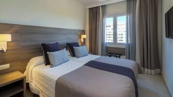 Una habitación de hotel con una cama grande, dos mesitas de noche, un televisor y una ventana con cortinas.
