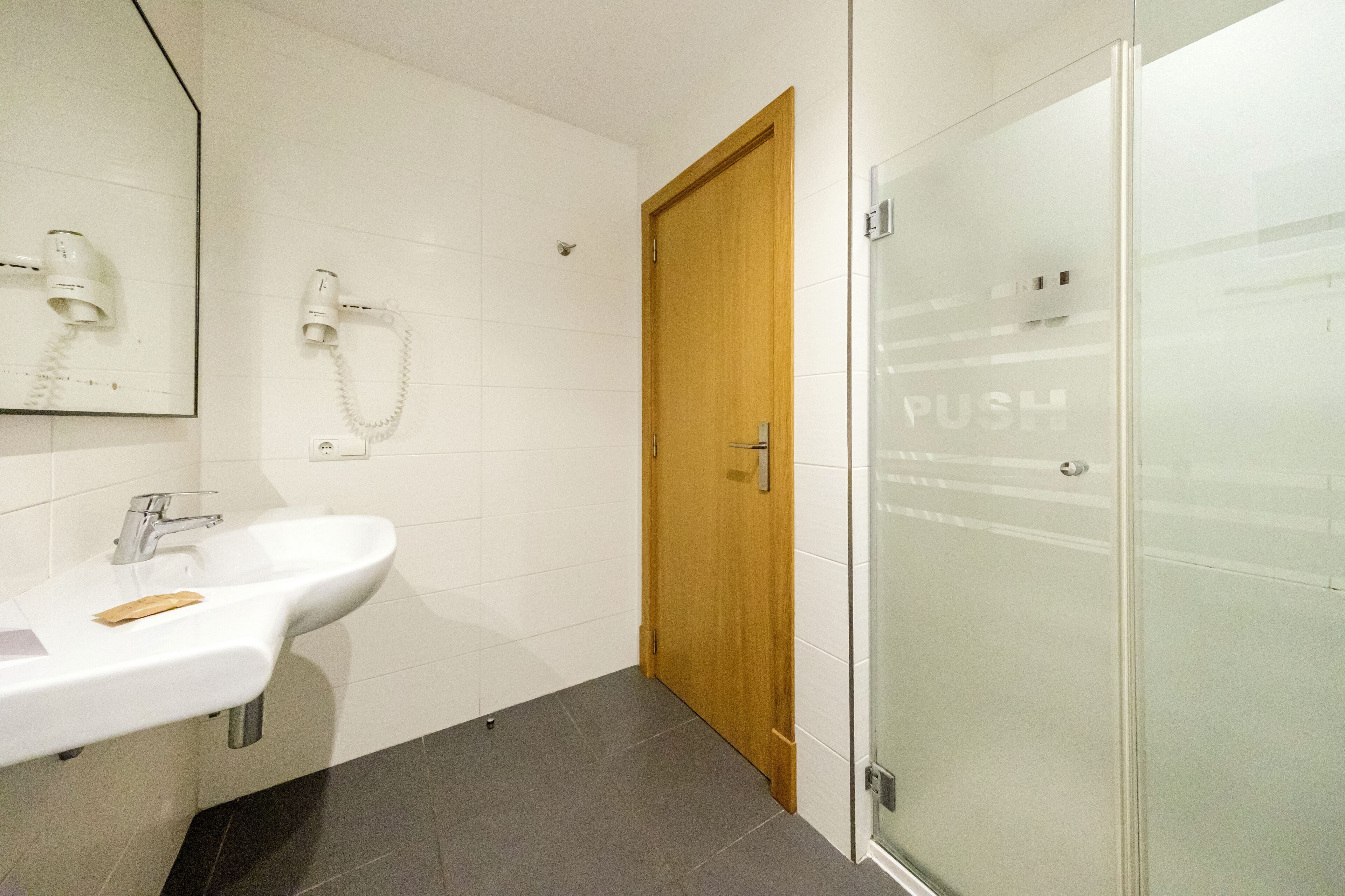 A bathroom with a white sink, a wooden door, and a glass shower enclosure.