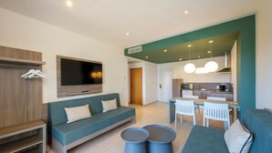 Una sala moderna con un sofá, dos mesitas redondas, un televisor y una kitchenette al fondo.