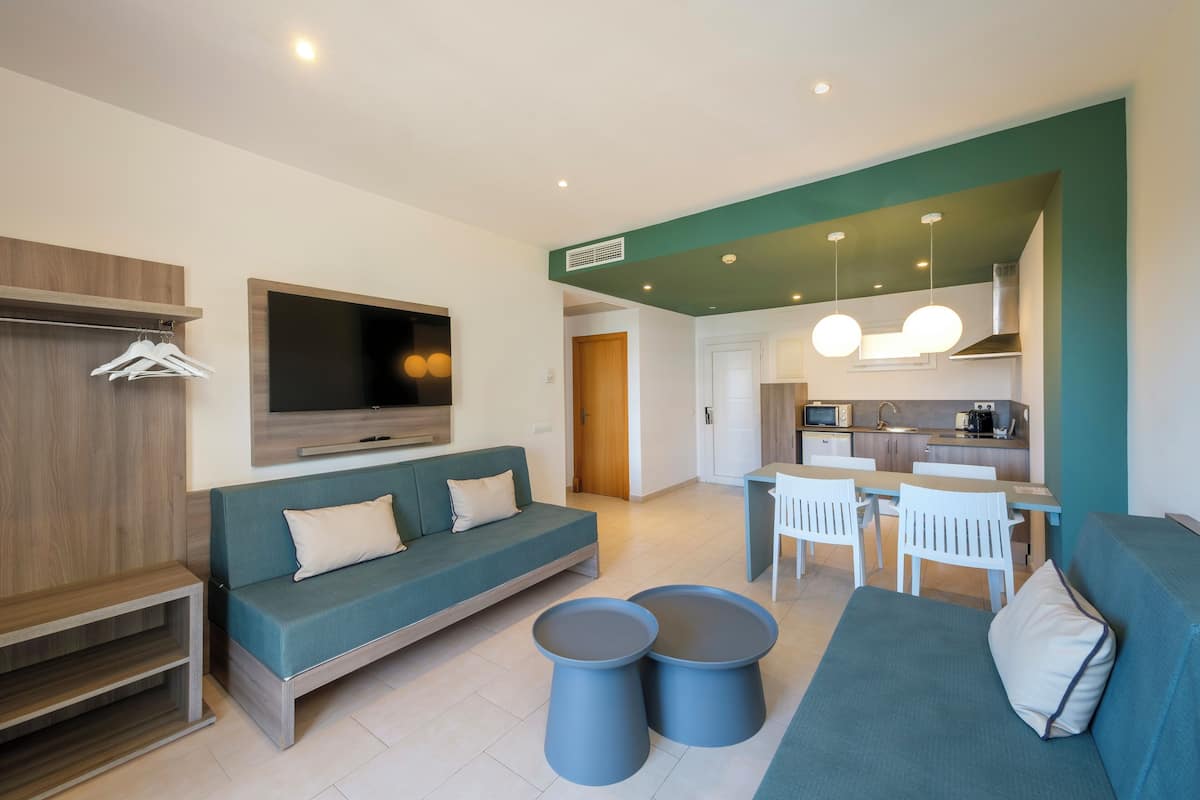 Een moderne woonkamer met een bank, twee ronde bijzettafels, een televisie en een kitchenette op de achtergrond.