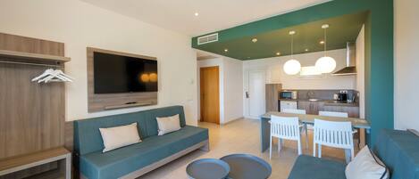 A modern living room with a sofa, two round side tables, a TV, and a kitchenette in the background.