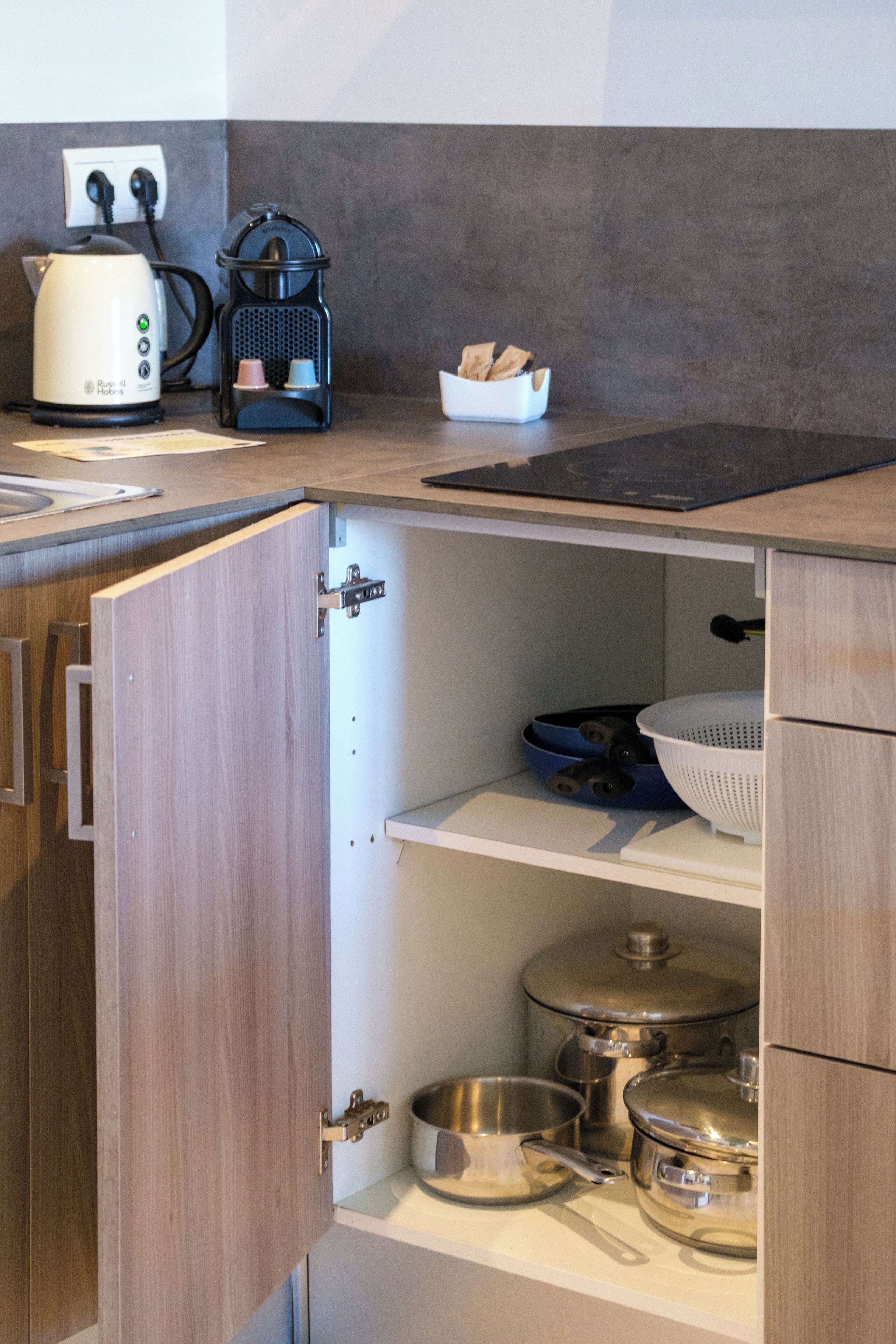 Una cocina con armarios de madera, cafetera, hervidor y diferentes ollas y sartenes.
