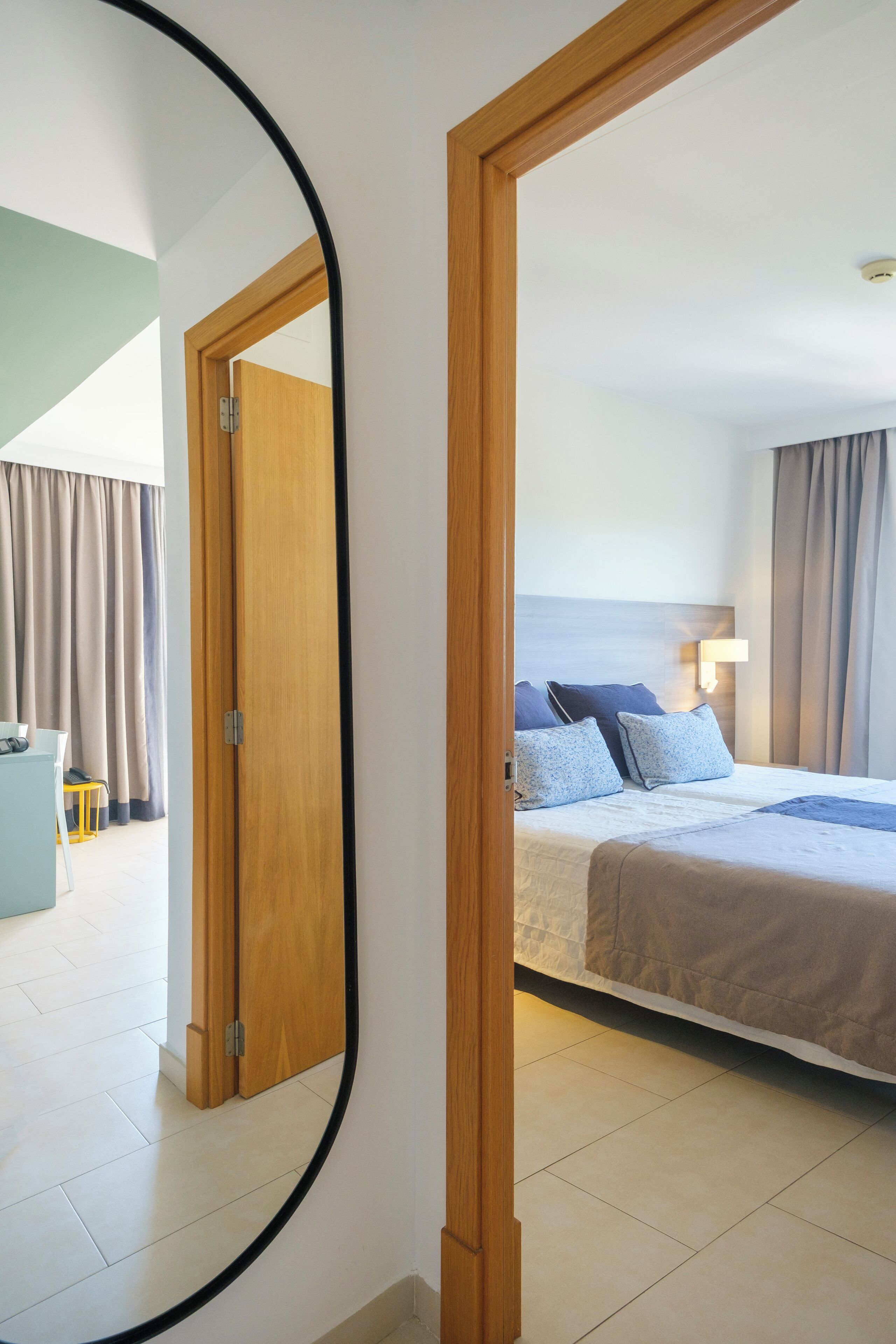 A hotel room with a bed, a bedside table, and a mirror reflecting the room.