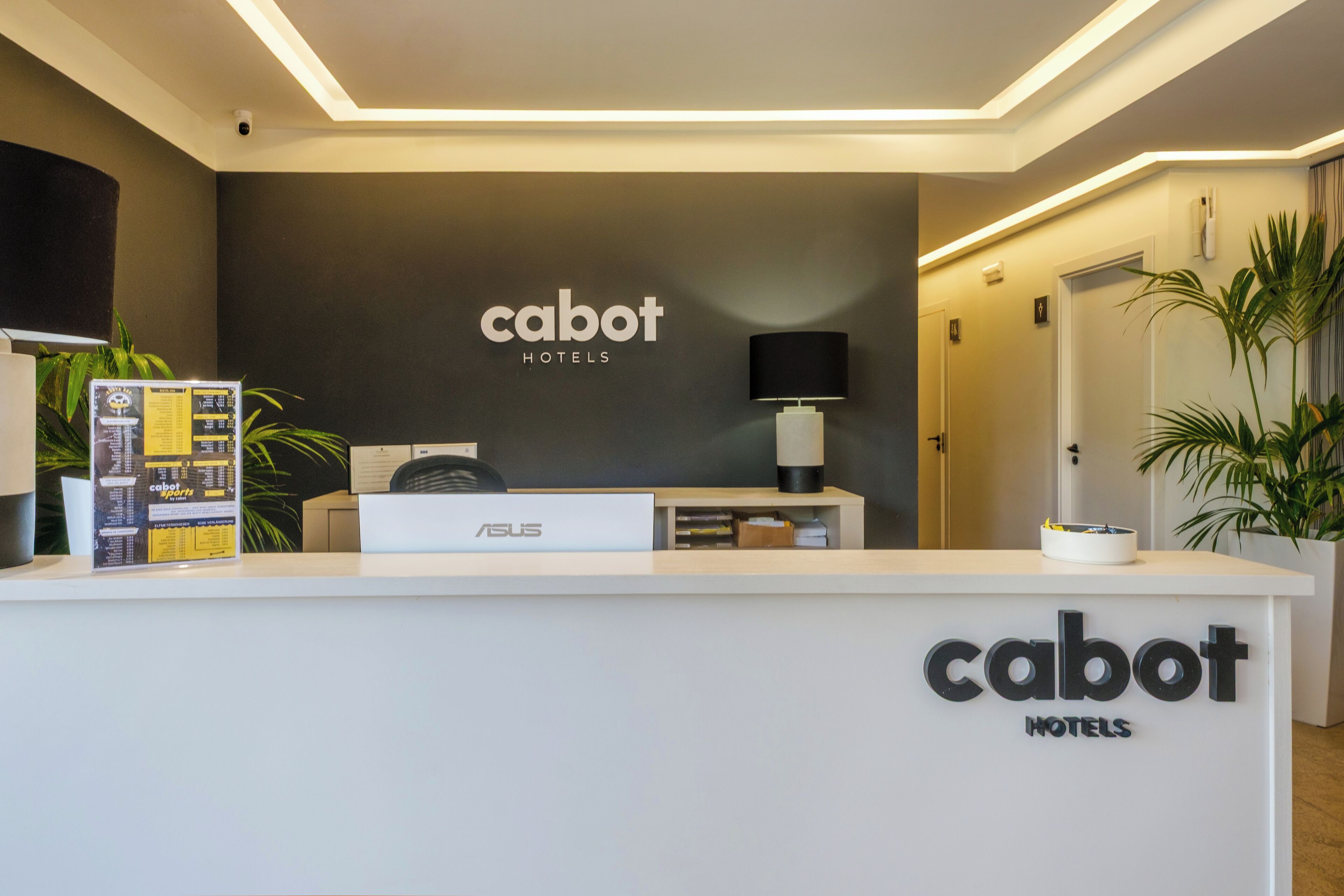 Un taulell de recepció d'hotel amb un cartell que diu "cabot hotels" i un ordinador ASUS.