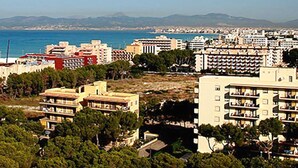 Un paisaje costero urbano con edificios residenciales densos, una vista despejada del mar y montañas al distante.