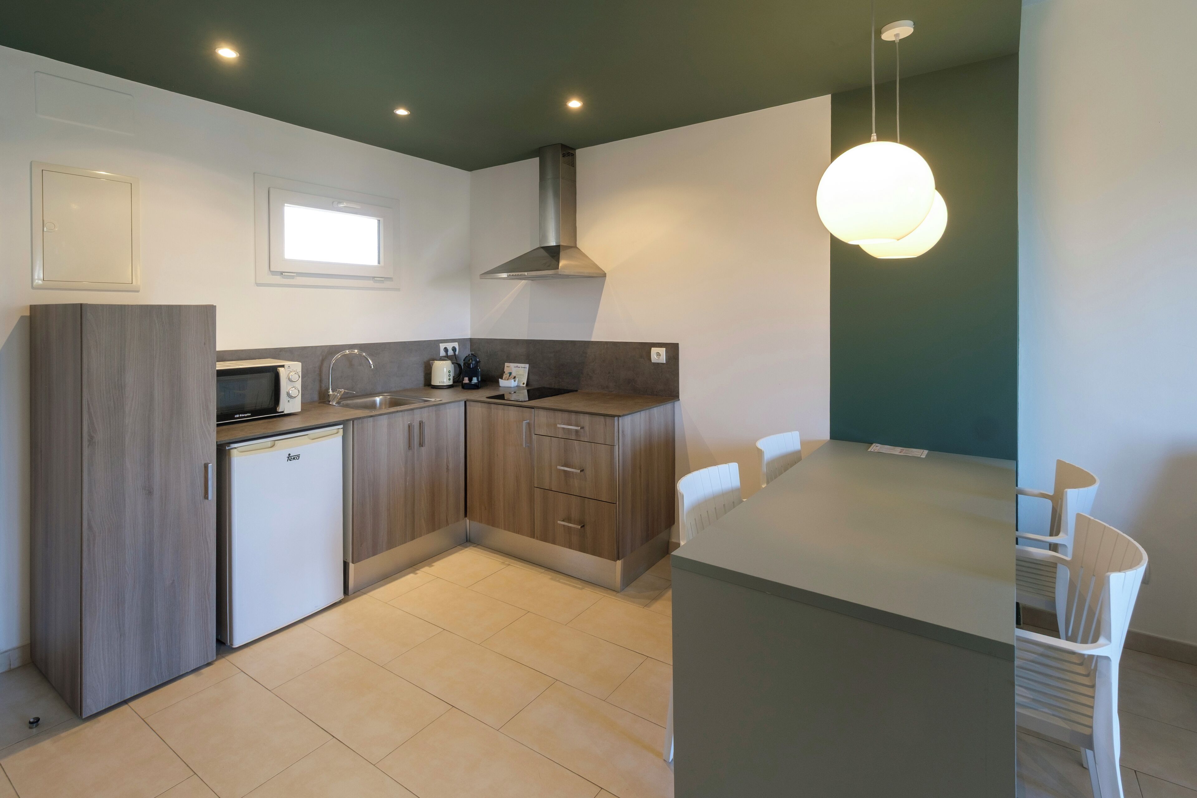 A modern kitchen with a built-in microwave, a sink, and a stove. There is a dining area with a table and chairs.
