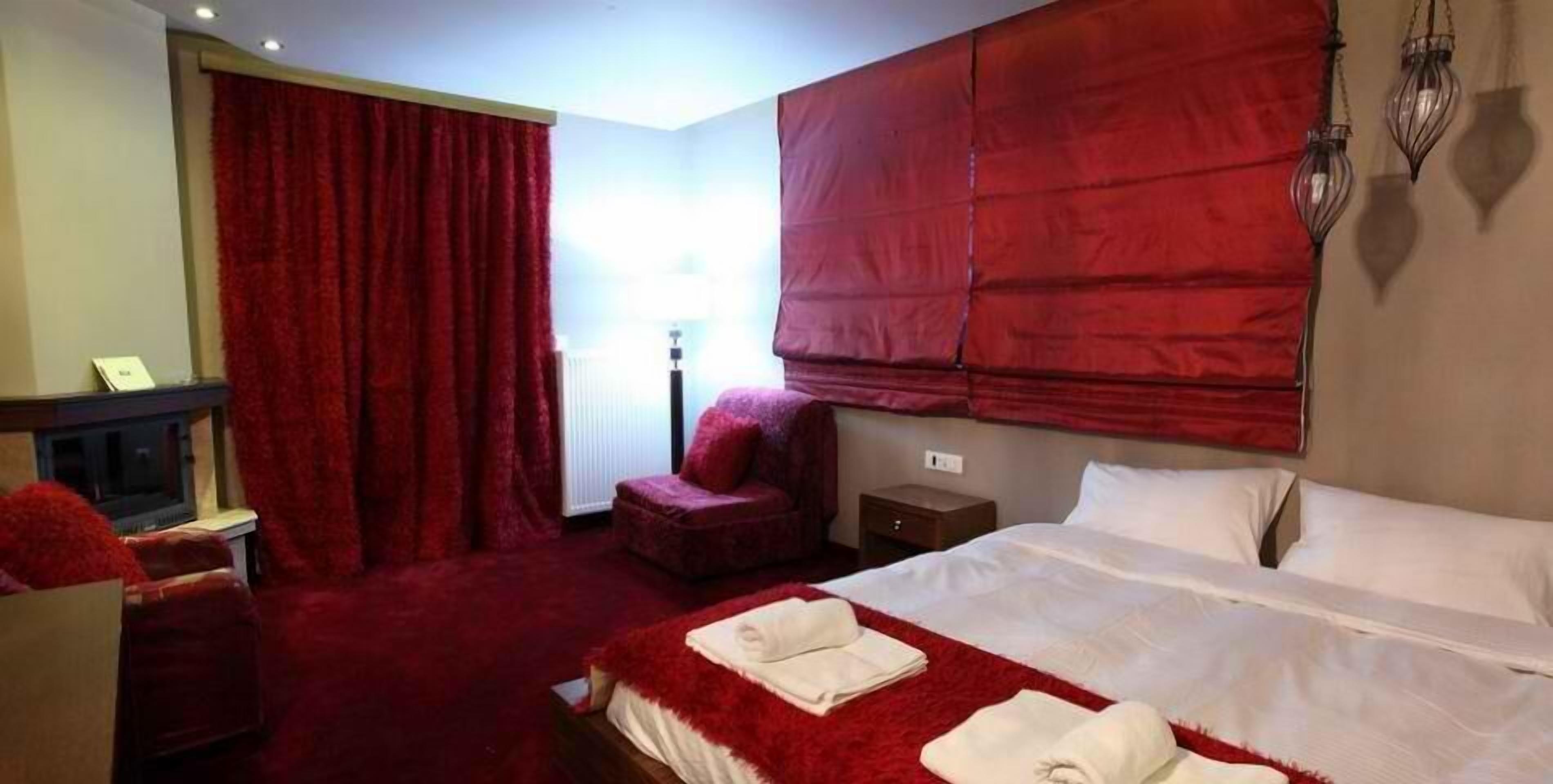 A hotel room with a large bed, red curtains, a small seating area, and a nightstand.