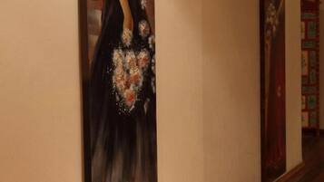 A hallway with a painting of a woman in a dress and a bookshelf in the background.