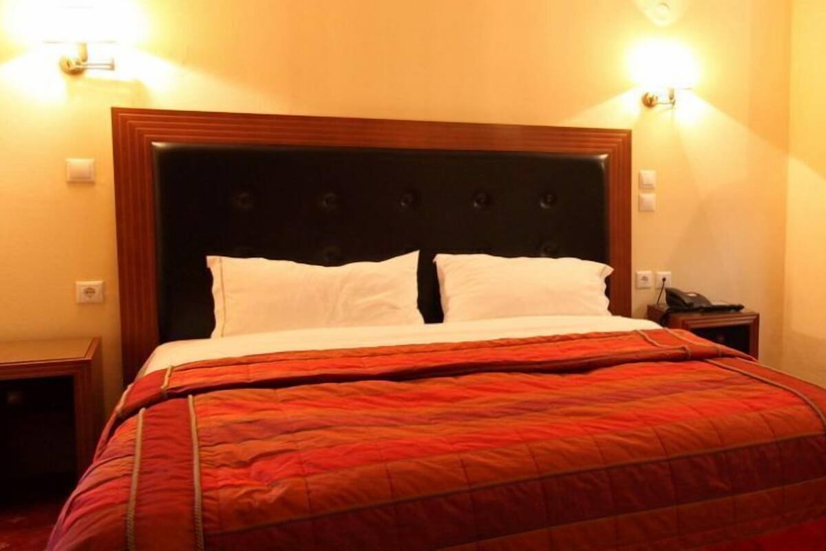 Une chambre d’hôtel avec un grand lit, deux tables de chevet, une petite table, une lampe et un lampadaire.