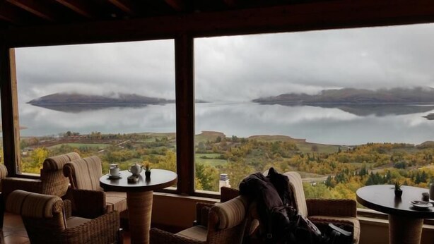 Ein Zimmer mit Korbmöbeln und Blick auf einen See und Hügel.