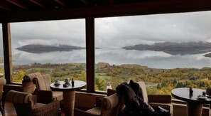 Une pièce meublée de mobilier en osier, avec vue sur un lac et des collines.